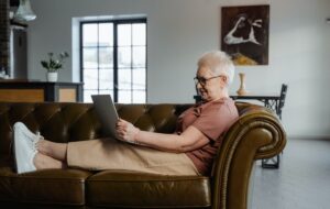 Elderly woman sitting on couch using laptop