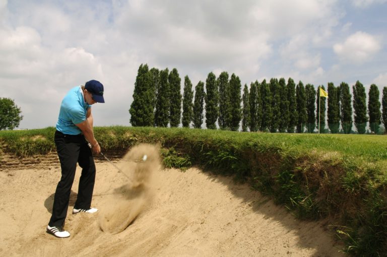 Golfer swinging out of a bunker