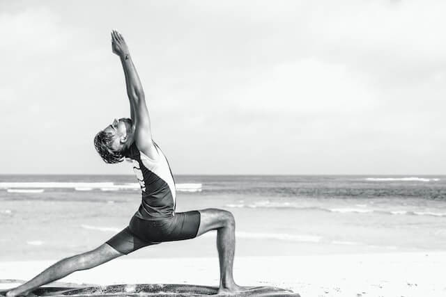 Man doing yoga on the beach, flexing healthy hips.