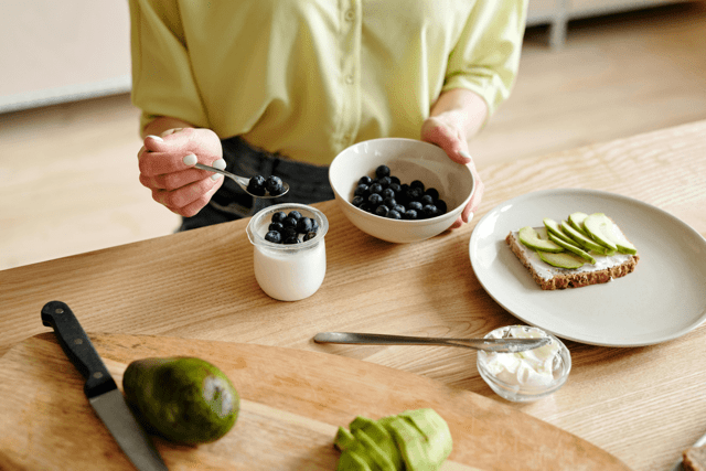 Close up of a woman adding blueberries to yogurt