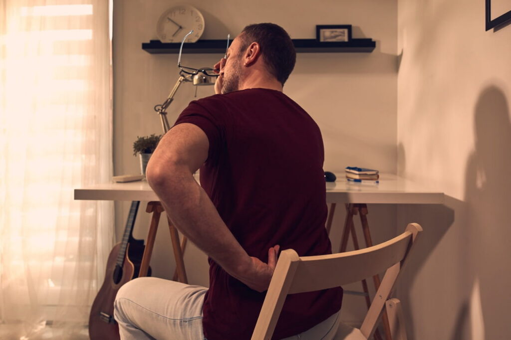 Man grabbing at his back as he sits in a chair