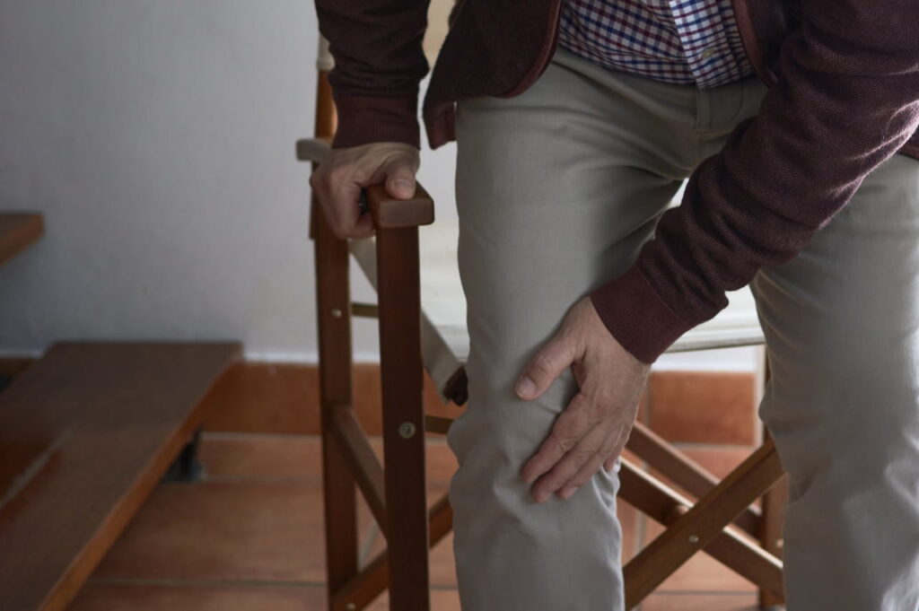 Elder man grabbing at his knee upon standing